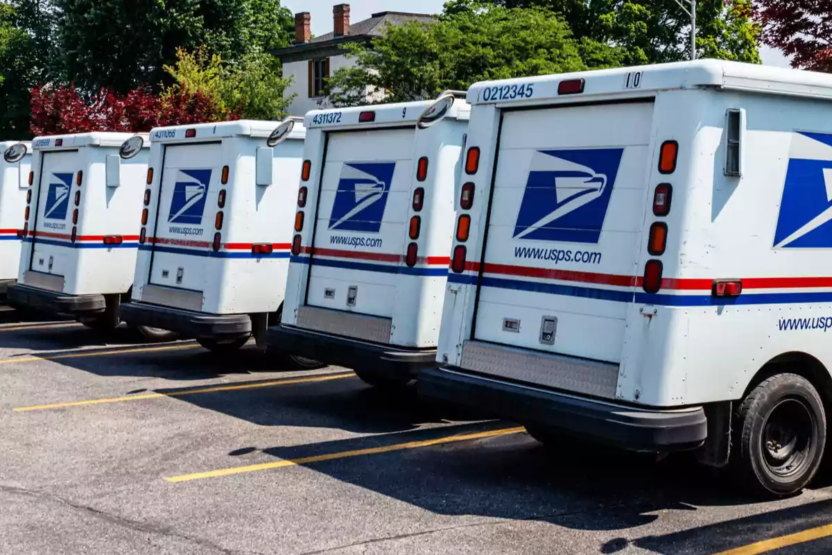 Camiones de reparto del servicio postal estacionados en fila en un aparcamiento.