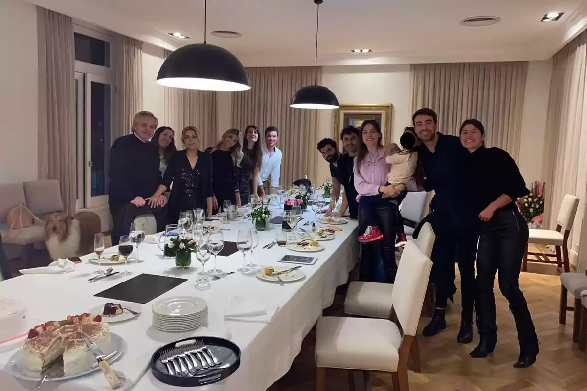 A group of people posing around a dining table with plates and glasses, in an elegant and well-lit setting.