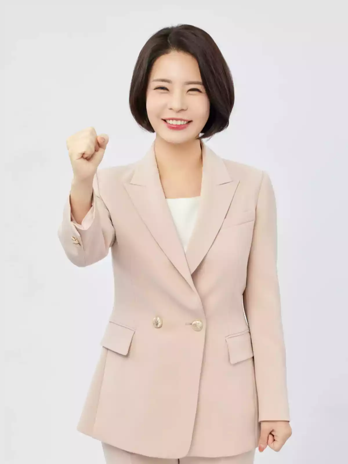 Smiling woman with short hair dressed in a beige suit making an encouraging gesture with her fist clenched