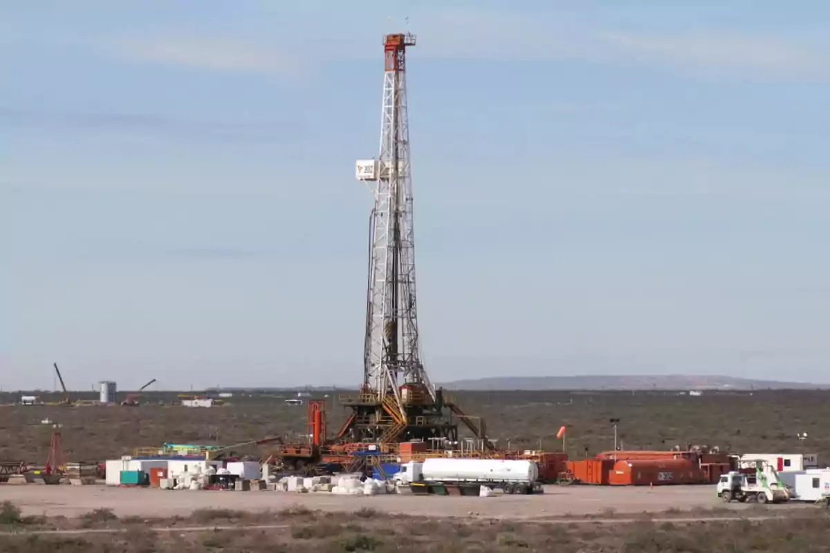 Una torre de perforación petrolera en un paisaje desértico con equipo y vehículos alrededor.