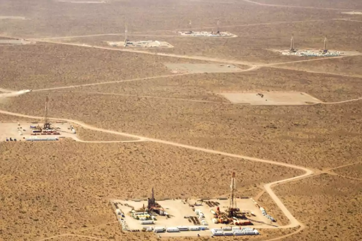 Vista aérea de un campo petrolero en un paisaje árido con varias plataformas de perforación distribuidas en el terreno.