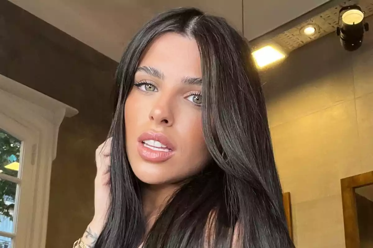 Una persona con cabello largo y oscuro mira a la cámara en un entorno interior.