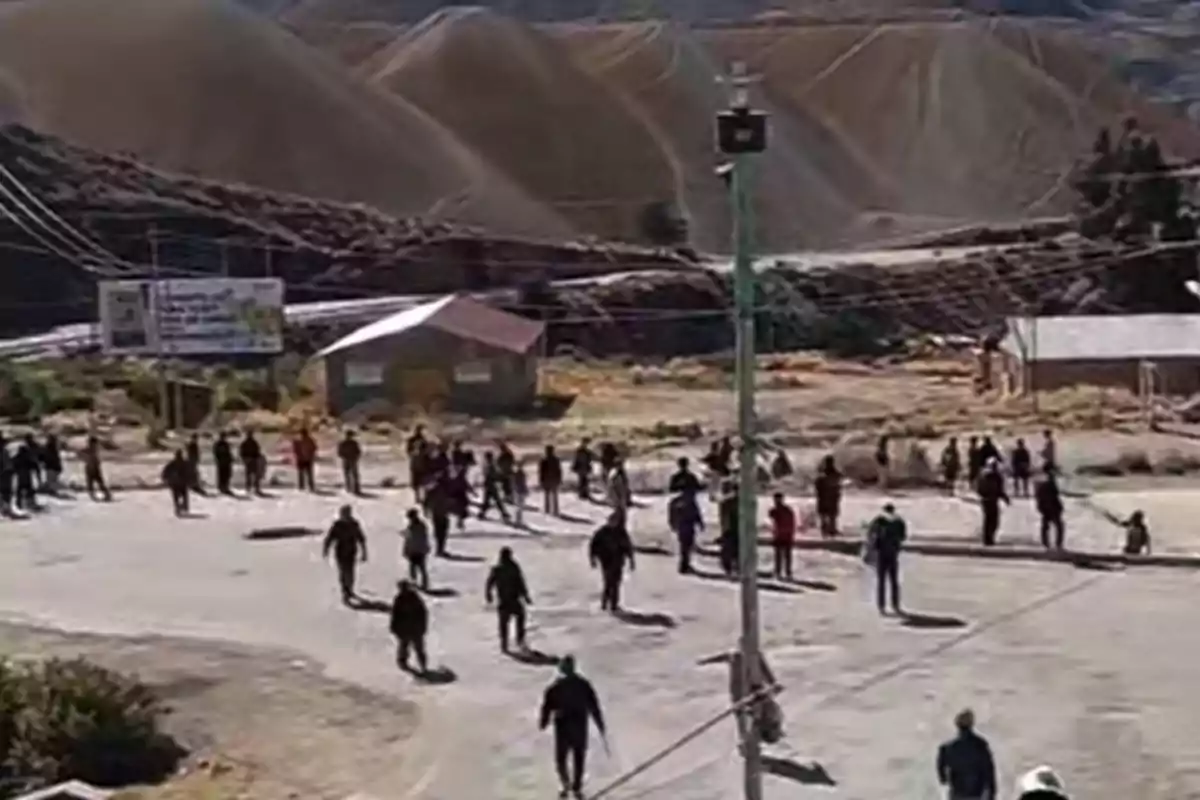 Several people are scattered along a street in a rural area with mountains in the background and some small houses around. Several people are scattered along a street in a rural area with mountains in the background and some small houses around.
