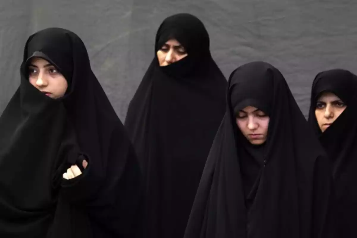 Four women dressed in black chador, some with their eyes closed, against a gray background.