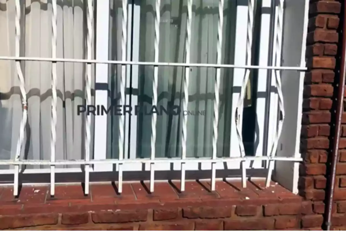 A window with white bars and curtains behind it on a brick wall. A window with white bars and curtains behind it on a brick wall.