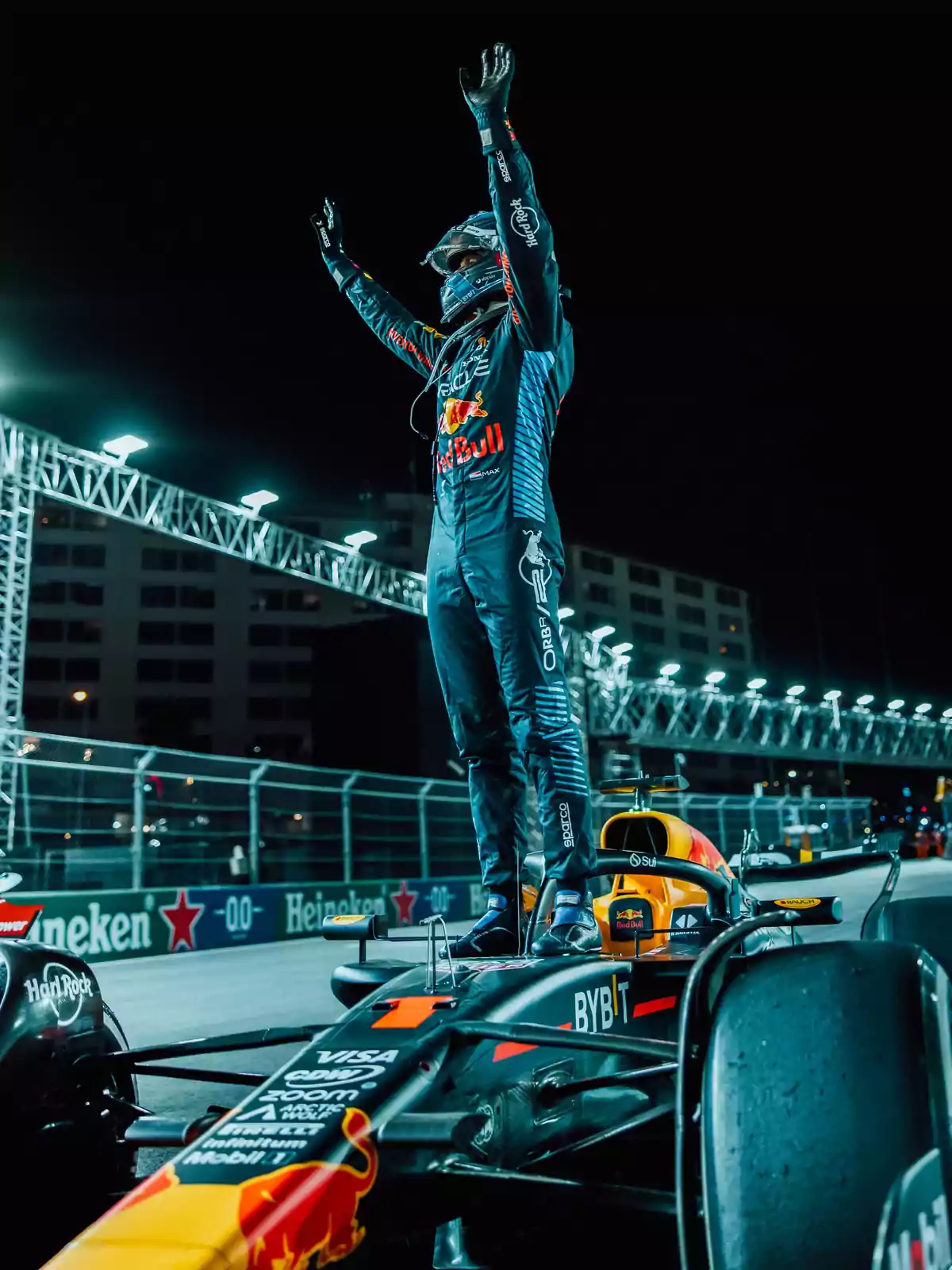 Un piloto de carreras celebra de pie sobre su auto en la pista durante la noche.