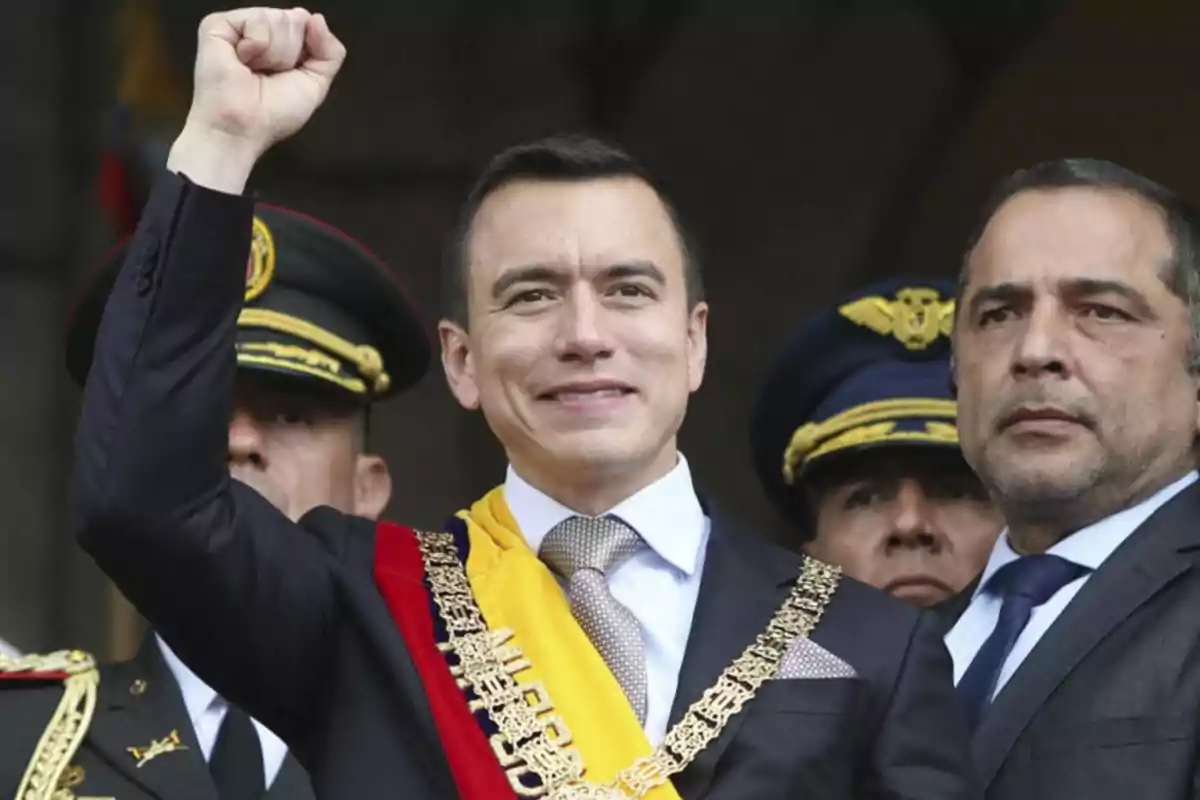 Un hombre con traje y banda presidencial levanta el puño rodeado de personas con uniformes militares.