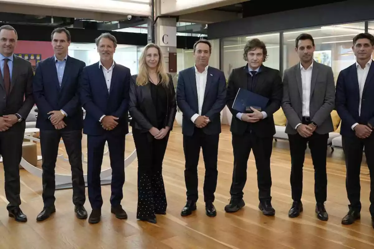 Un grupo de personas vestidas formalmente posan en una oficina moderna con suelos de madera y un fondo de paredes de cristal. Un grupo de personas vestidas formalmente posan en una oficina moderna con suelos de madera y un fondo de paredes de cristal.