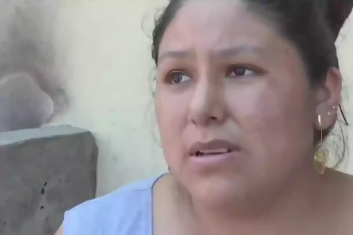 Una mujer con expresión seria y aretes dorados está mirando hacia un lado.