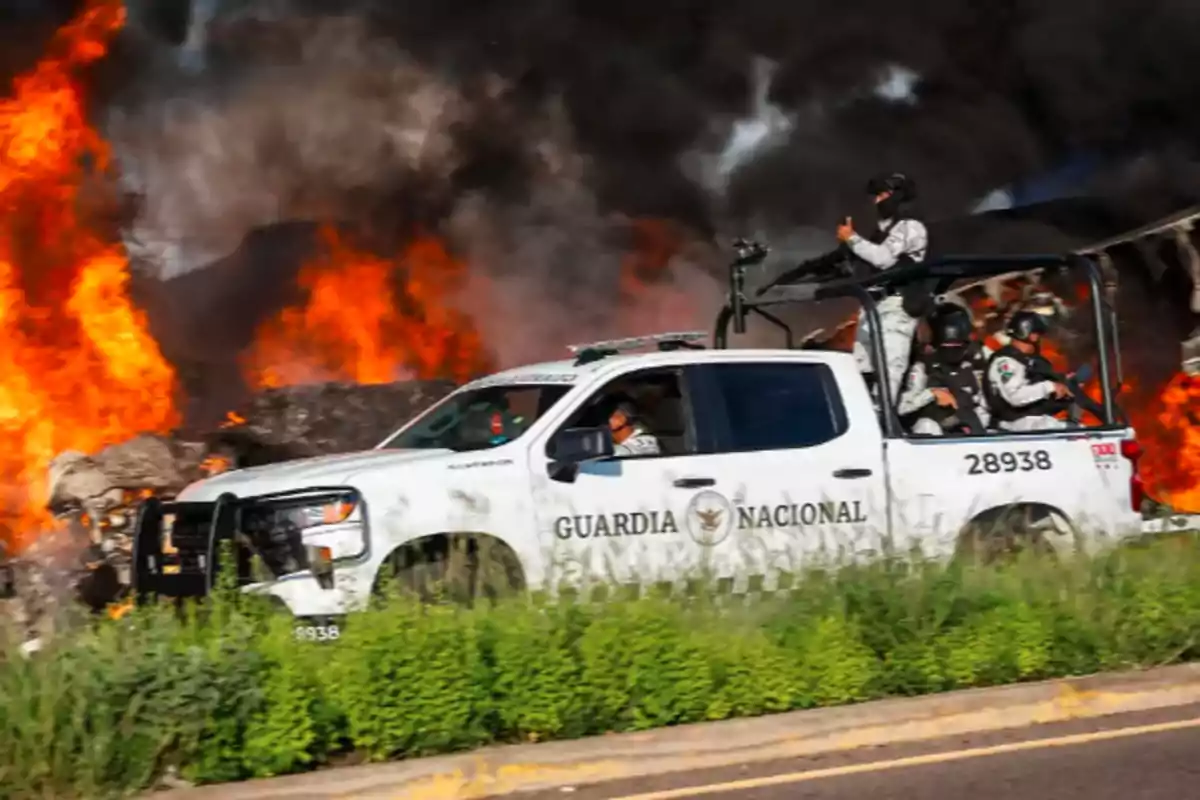 Vehículo de la Guardia Nacional frente a un incendio con llamas intensas en el fondo.