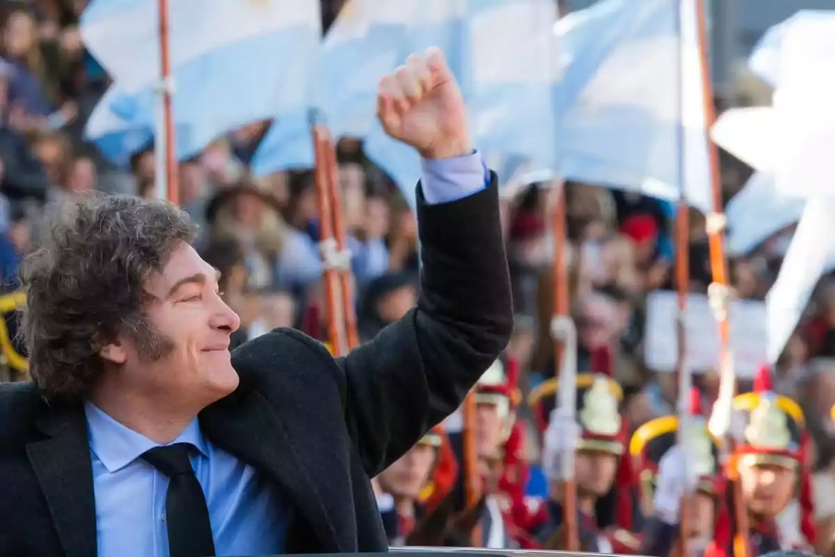 Un hombre sonriente levanta el puño en un evento con banderas argentinas de fondo.