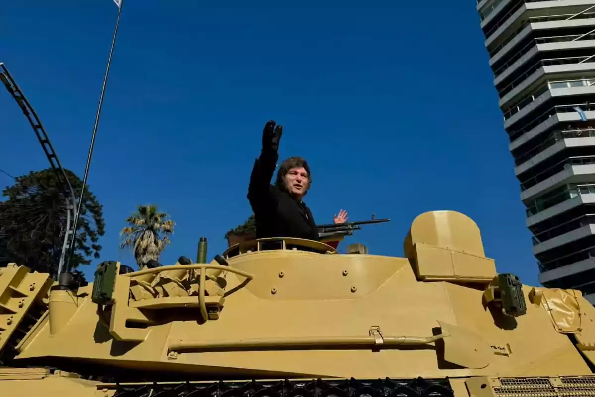 A person waving from a military vehicle in an urban setting with a clear sky. A person waving from a military vehicle in an urban setting with a clear sky.