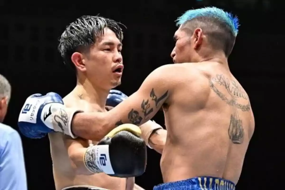 Dos boxeadores en el ring durante un combate, uno con guantes azules y el otro con guantes negros, ambos mostrando tatuajes en sus cuerpos. Dos boxeadores en el ring durante un combate, uno con guantes azules y el otro con guantes negros, ambos mostrando tatuajes en sus cuerpos.