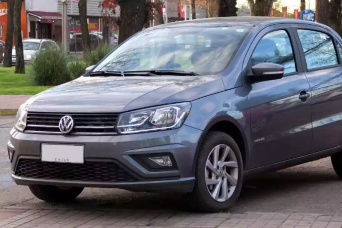 Un automóvil Volkswagen gris estacionado en una calle con árboles y edificios al fondo.