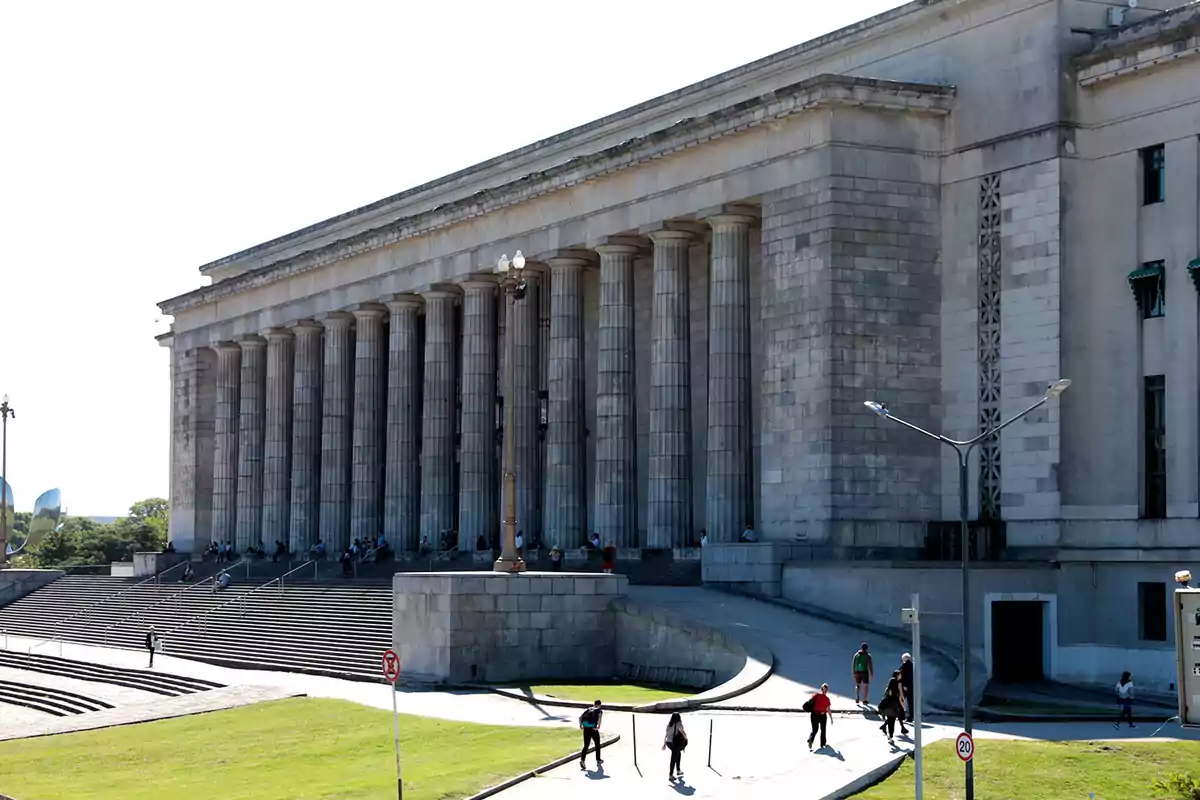 Building with classical columns and a wide staircase where several people walk and sit on the steps.