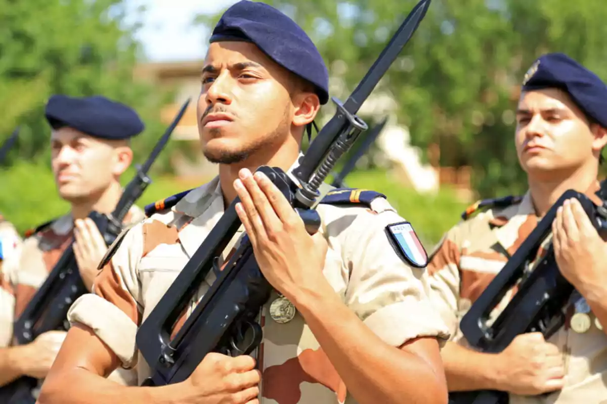 Soldados en uniforme camuflado sosteniendo rifles con bayonetas durante una ceremonia al aire libre.