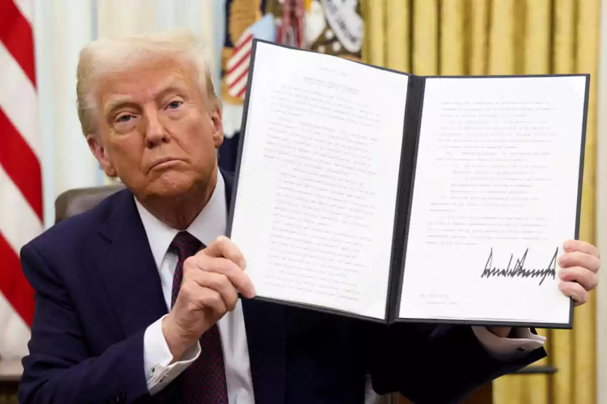 Un hombre de traje oscuro sostiene un documento abierto con texto y una firma visible en una oficina con una bandera de fondo. Un hombre de traje oscuro sostiene un documento abierto con texto y una firma visible en una oficina con una bandera de fondo.