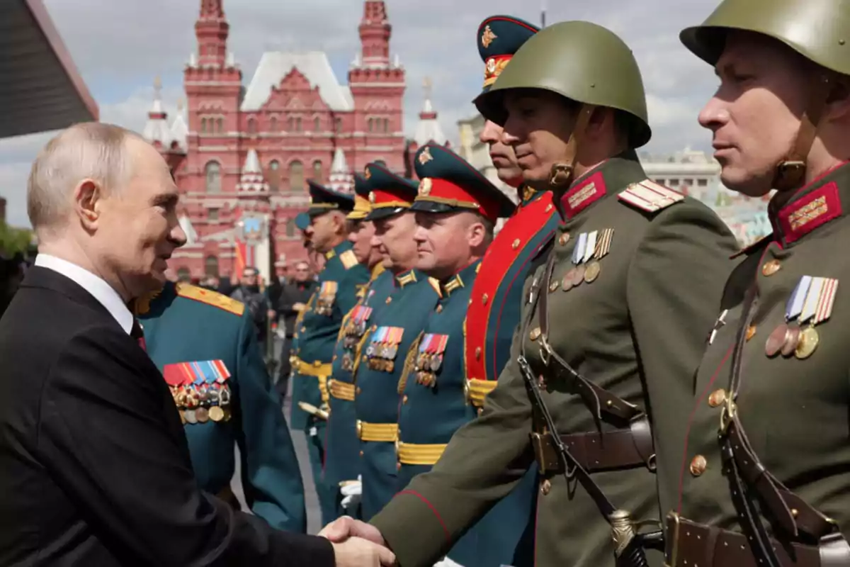 Un hombre de traje oscuro estrecha la mano de un militar uniformado frente a un grupo de soldados con medallas, con un edificio histórico de fondo. Un hombre de traje oscuro estrecha la mano de un militar uniformado frente a un grupo de soldados con medallas, con un edificio histórico de fondo.