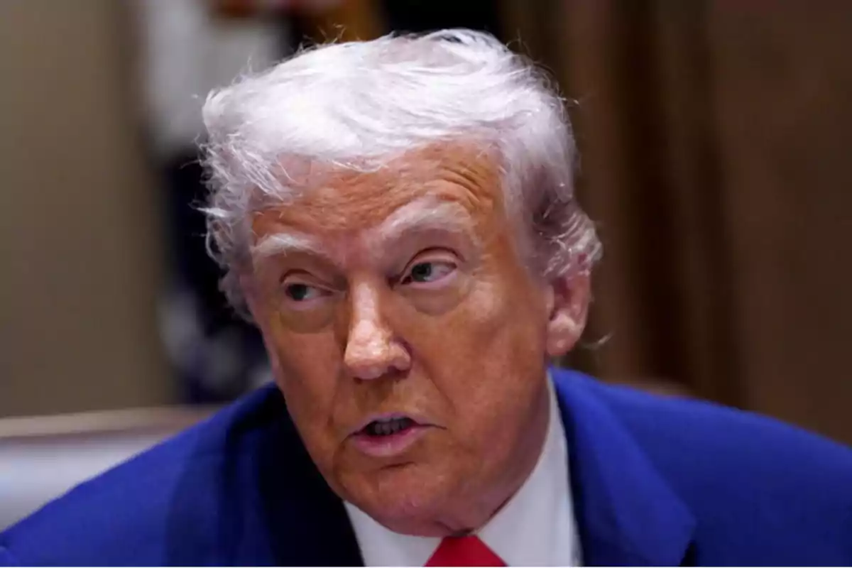 Gray-haired, tanned-skinned man wearing a blue jacket and red tie looking to the side