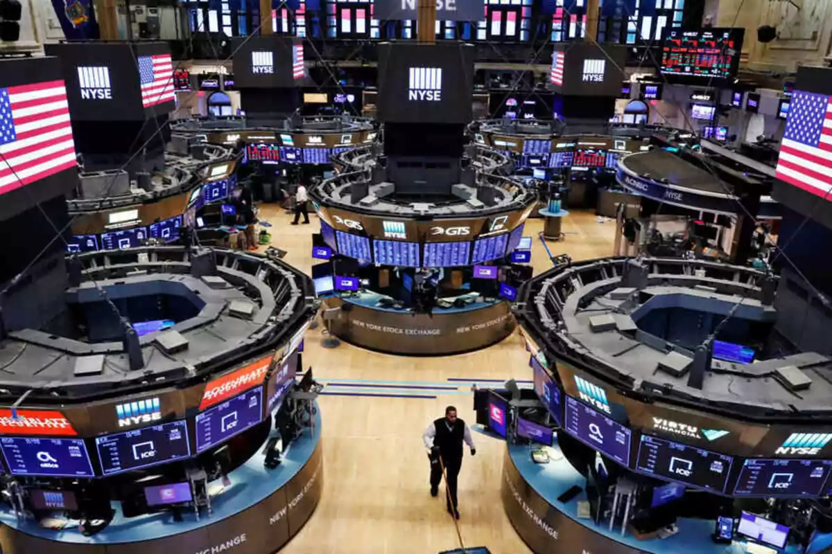 Interior of the New York Stock Exchange with several circular workstations and electronic screens displaying financial information.