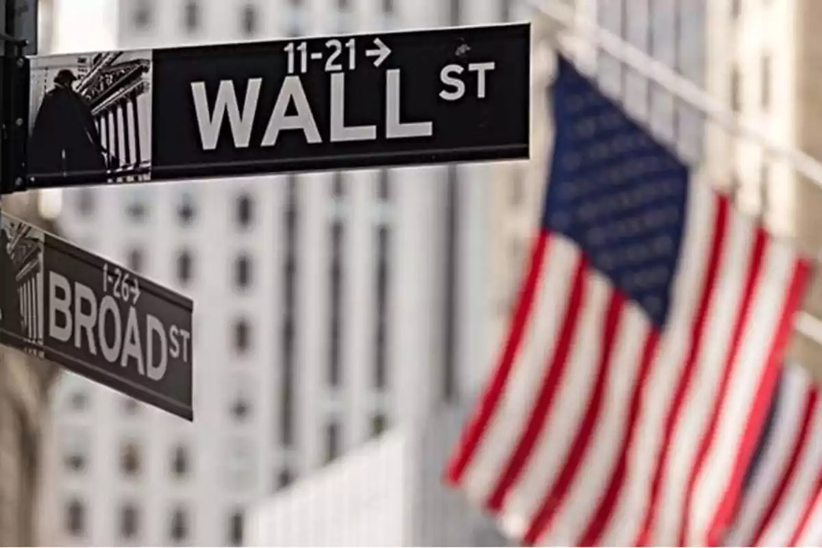 Señal de las calles Wall Street y Broad Street con una bandera de Estados Unidos al fondo.