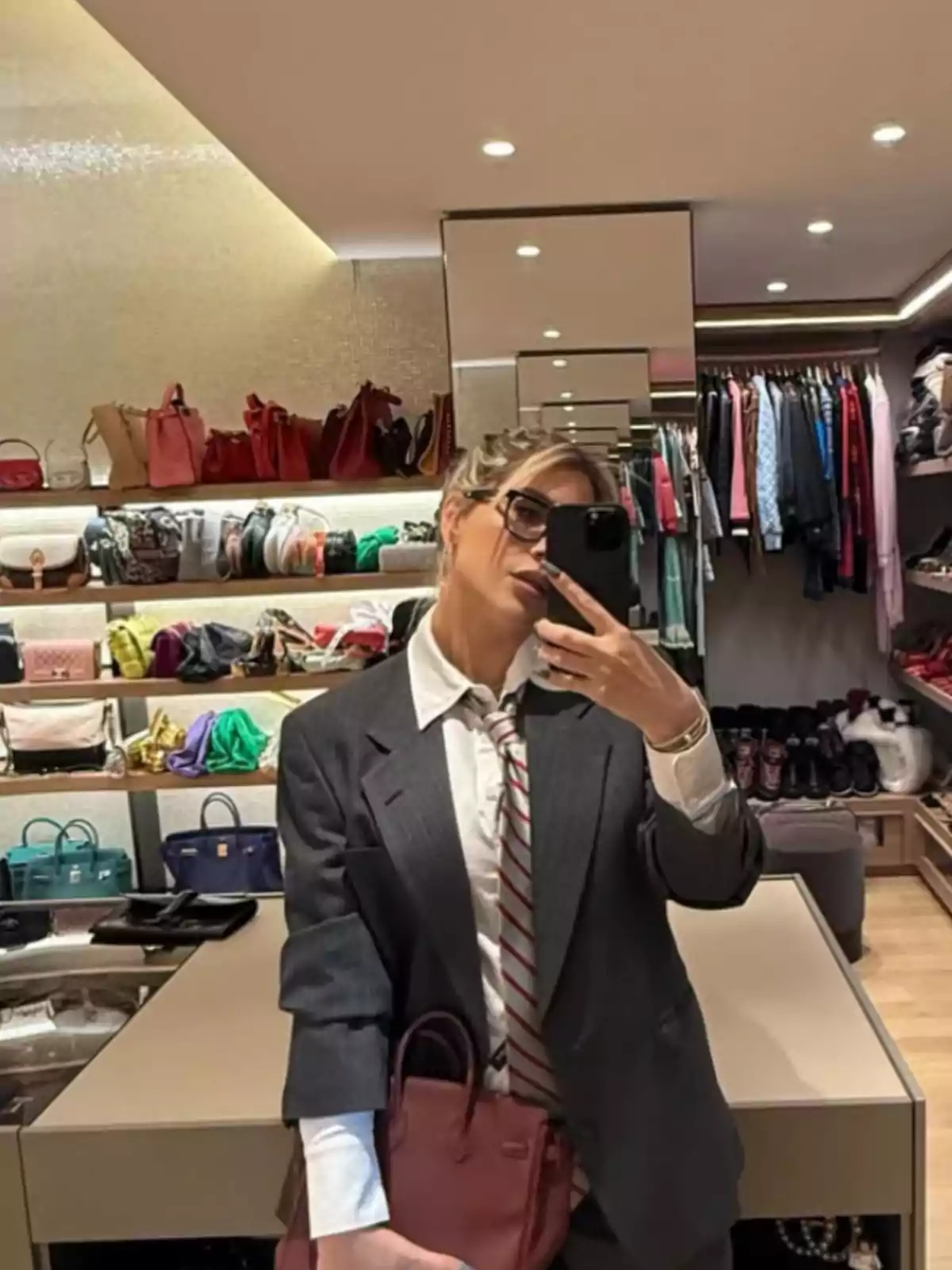 Persona tomándose una selfie en un vestidor elegante con muchas bolsas y ropa organizada en estantes y percheros Persona tomándose una selfie en un vestidor elegante con muchas bolsas y ropa organizada en estantes y percheros