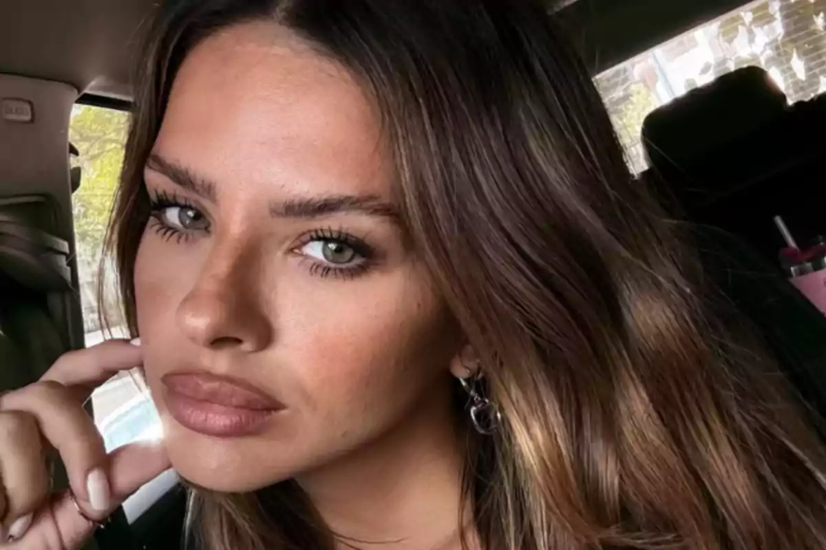 Mujer de cabello largo y castaño con ojos claros sentada en un automóvil mirando a la cámara con expresión seria