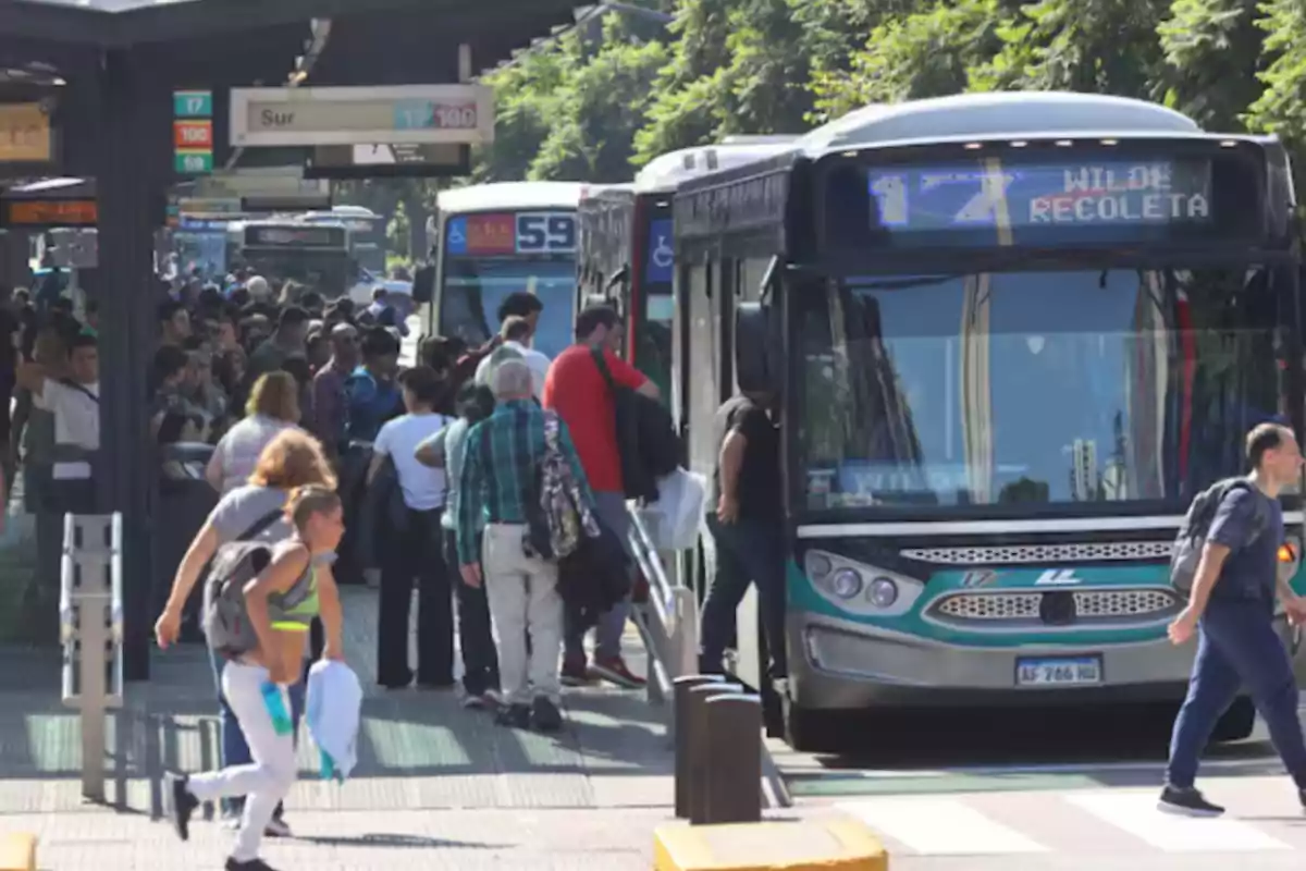 People lining up to board a bus at a busy station during the day.