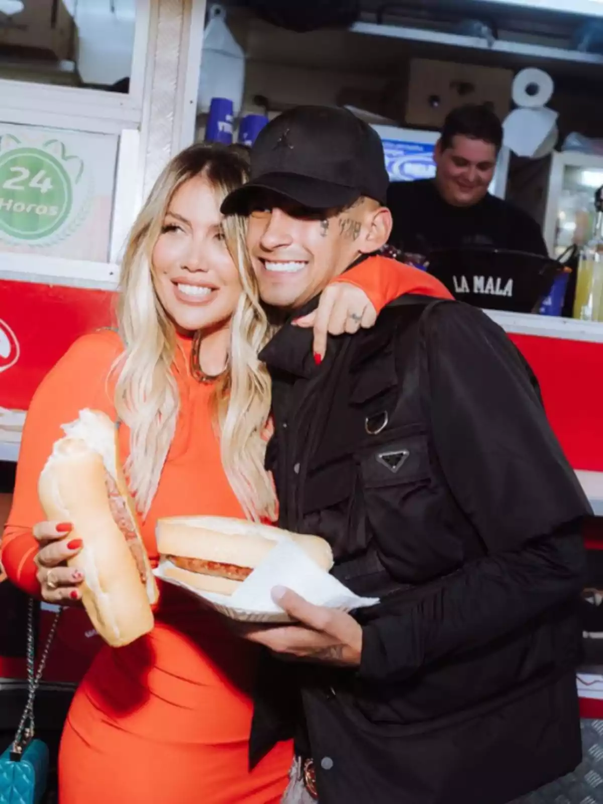 A smiling couple holds snacks in front of a food stand while a man works in the background. A smiling couple holds snacks in front of a food stand while a man works in the background.