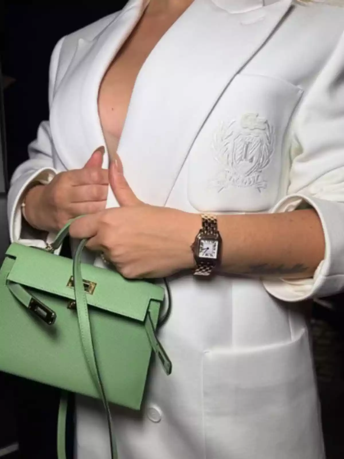 A person with a white blazer, holding a green handbag, and wearing a wristwatch. A person with a white blazer, holding a green handbag, and wearing a wristwatch.