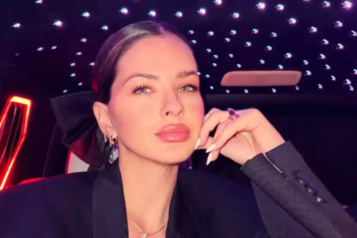 A person with tied-up hair and subtle makeup, dressed in black, poses in an environment with bright lights on the ceiling. A person with tied-up hair and subtle makeup, dressed in black, poses in an environment with bright lights on the ceiling.