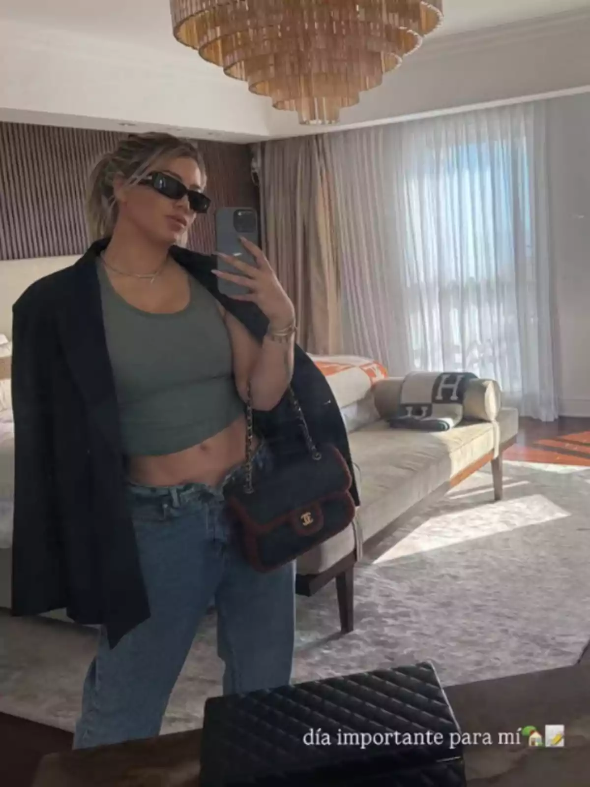 A person taking a selfie in front of a mirror in an elegant room, wearing sunglasses, a green top, a black jacket, jeans, and holding a designer handbag. A person taking a selfie in front of a mirror in an elegant room, wearing sunglasses, a green top, a black jacket, jeans, and holding a designer handbag.