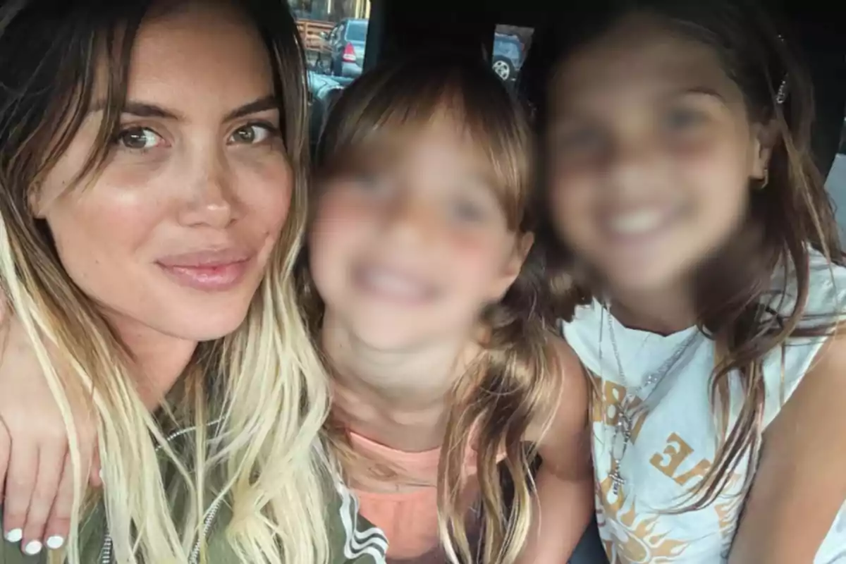 A woman smiles next to two girls inside a car, the girls' faces are blurred.