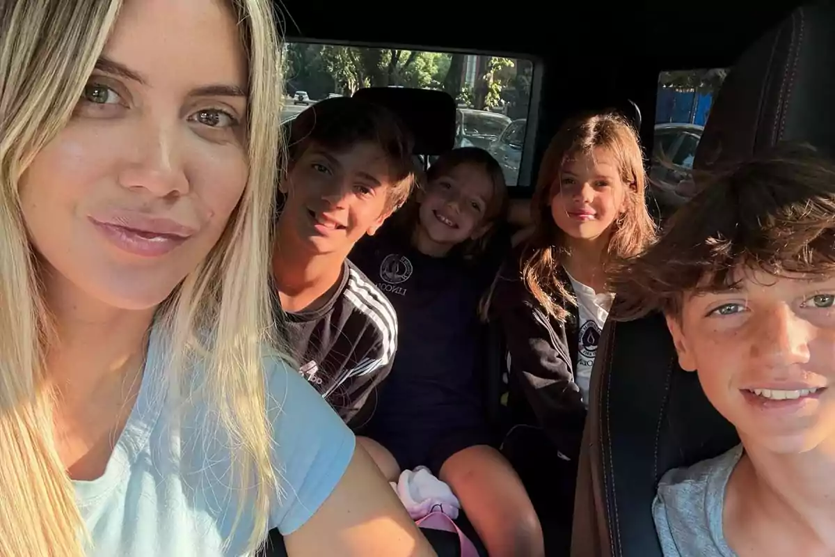 A blonde woman smiles next to four children inside a car.