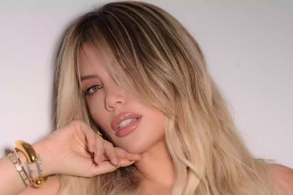 Una persona con cabello rubio y maquillaje sutil posa con la mano cerca del rostro.