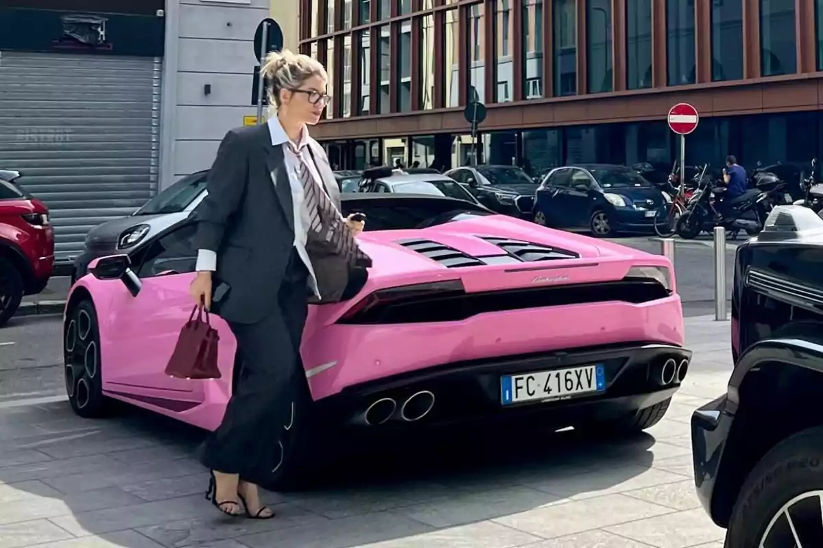 Mujer con traje formal y gafas camina junto a un Lamborghini rosa estacionado en una calle urbana Mujer con traje formal y gafas camina junto a un Lamborghini rosa estacionado en una calle urbana