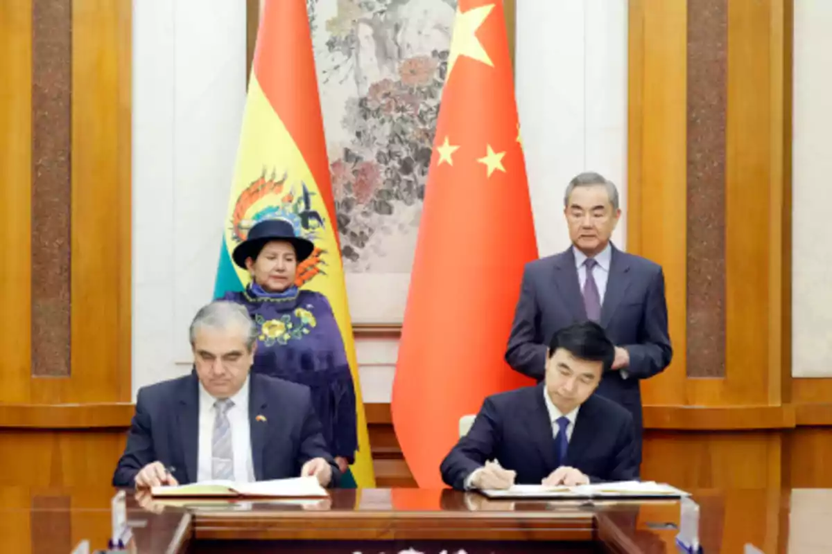 Personas en una ceremonia de firma de documentos con las banderas de Bolivia y China de fondo.