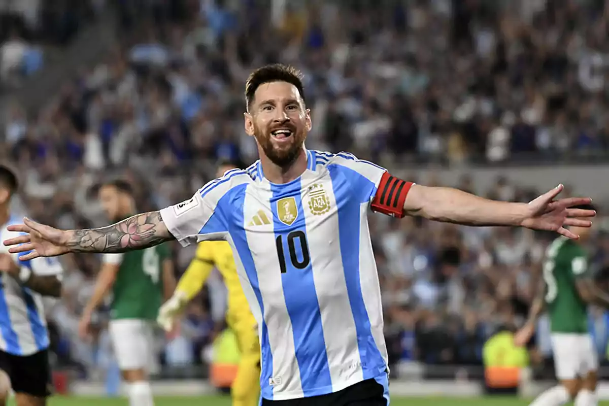 Un jugador de fútbol con uniforme de Argentina celebra con los brazos abiertos en un estadio lleno de espectadores. Un jugador de fútbol con uniforme de Argentina celebra con los brazos abiertos en un estadio lleno de espectadores.