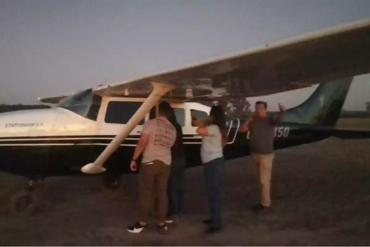 Personas revisando un avión pequeño en un campo al atardecer.