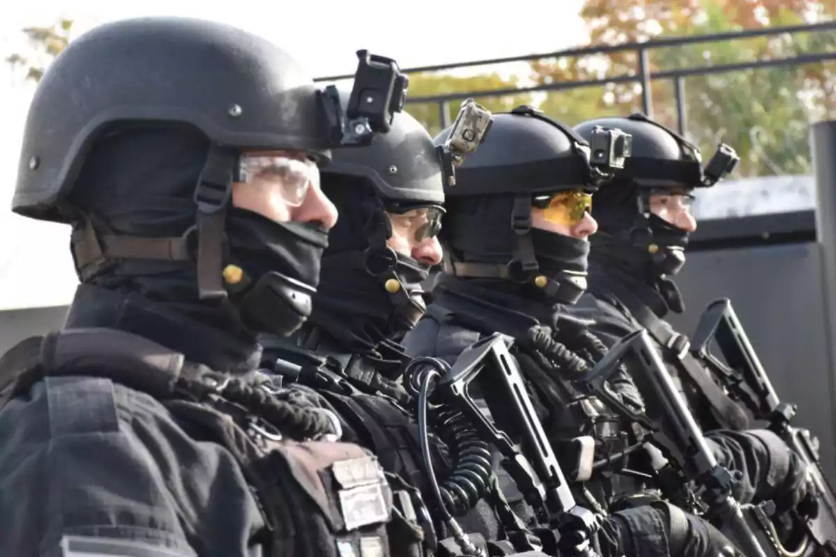 Grupo de agentes tácticos con equipo de protección y armas en formación.