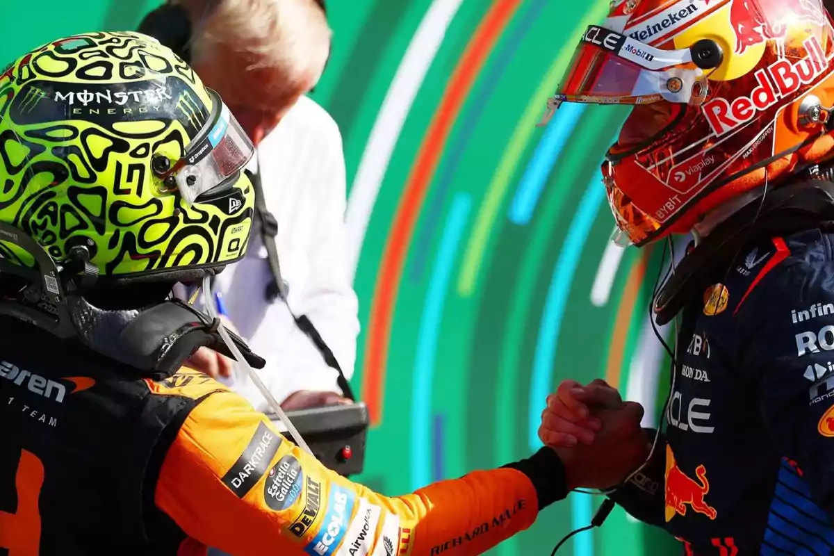 Dos pilotos de Fórmula 1 se dan la mano mientras llevan puestos sus cascos y trajes de carreras, uno con un casco amarillo y negro y el otro con un casco rojo y azul.