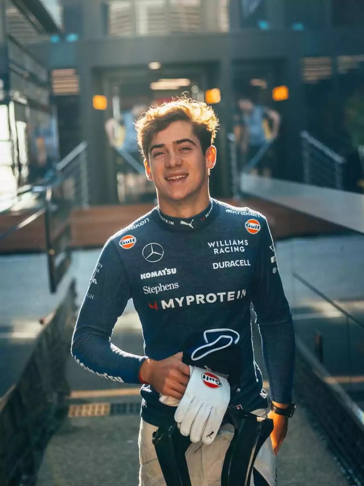 Un joven con uniforme de carreras de la escudería Williams Racing sonríe a la cámara.