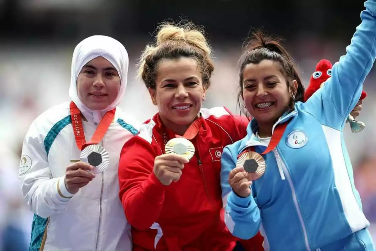 Tres atletas femeninas sonríen mientras muestran sus medallas.