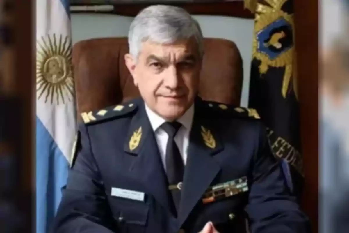 Hombre de cabello canoso con uniforme de policía sentado en un escritorio con la bandera de Argentina detrás Hombre de cabello canoso con uniforme de policía sentado en un escritorio con la bandera de Argentina detrás