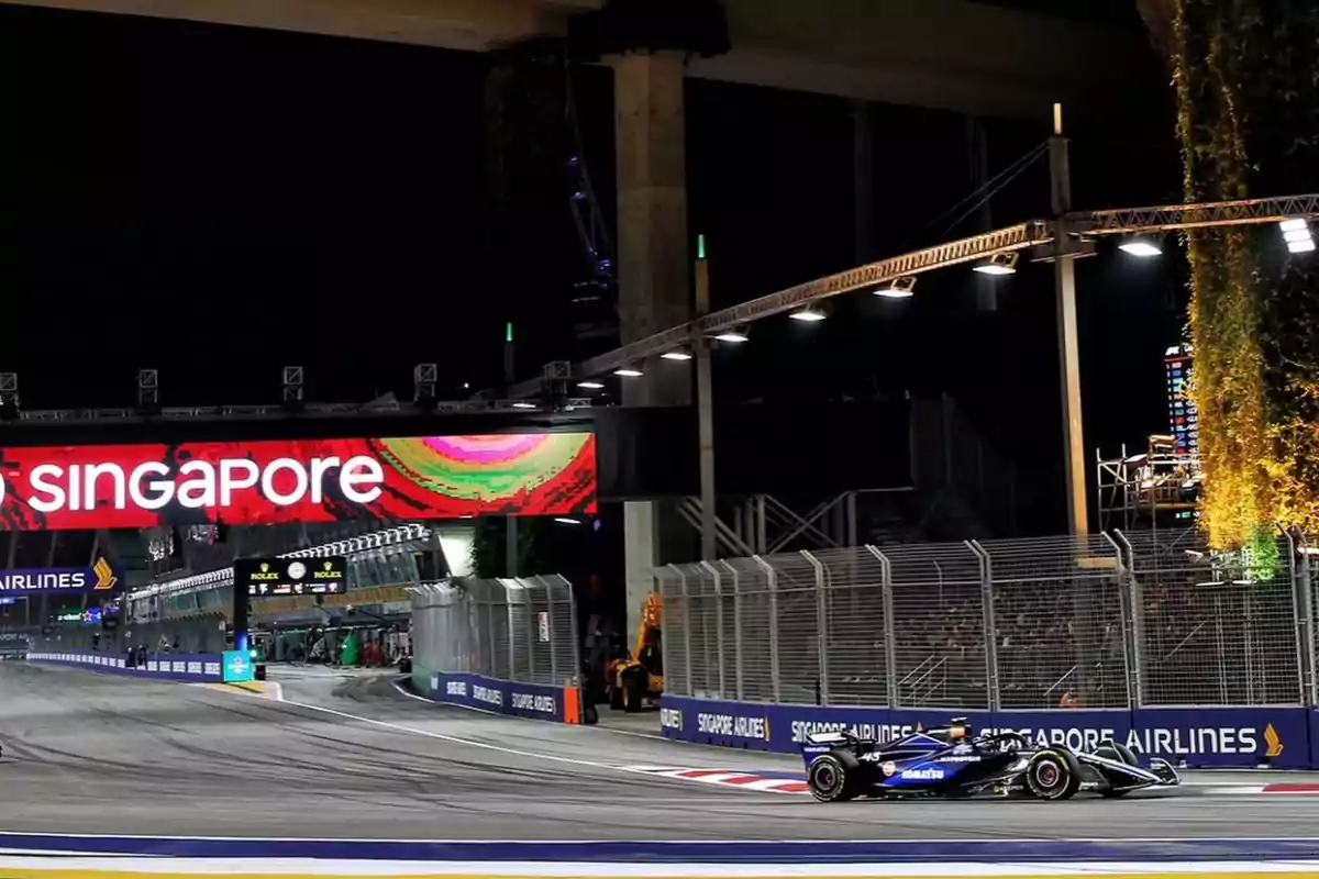 Un coche de carreras en un circuito nocturno con un cartel que dice "Singapore" en el fondo.