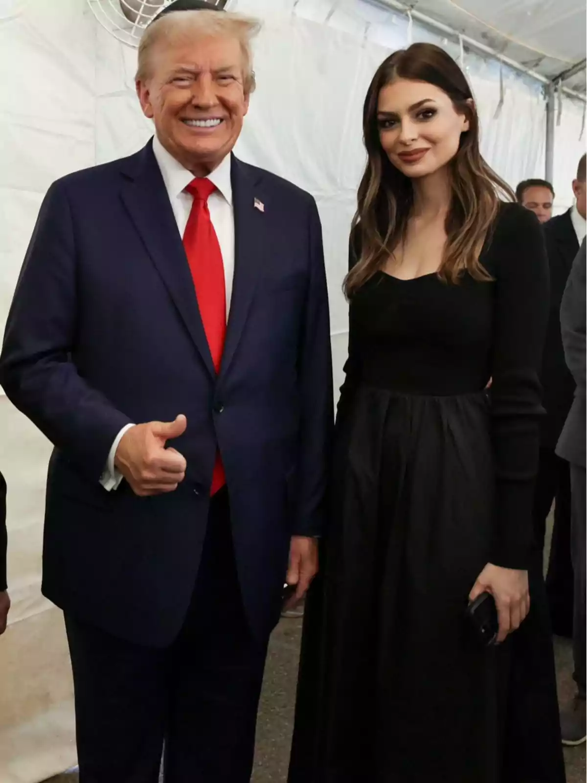 Dos personas posando juntas en un evento formal, una de ellas lleva un traje oscuro con corbata roja y la otra un vestido negro.