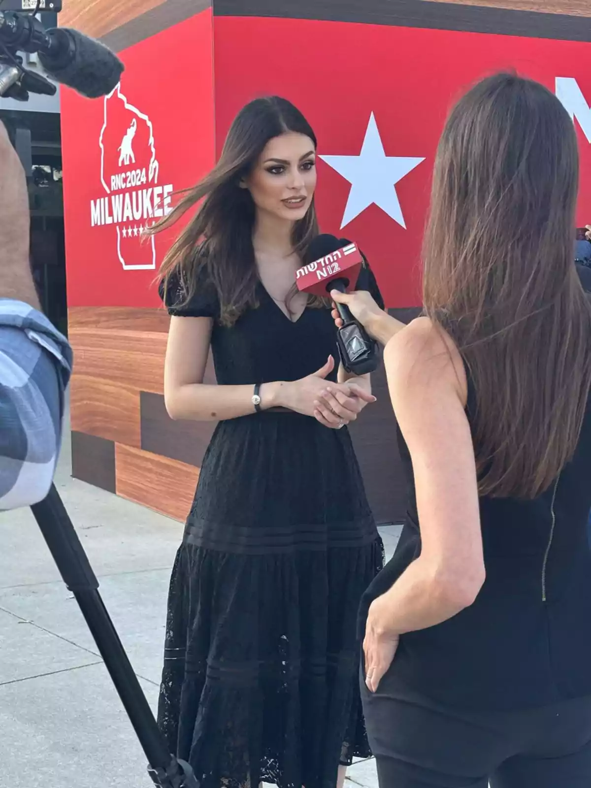 Una mujer vestida de negro es entrevistada por una reportera frente a un cartel rojo que dice 