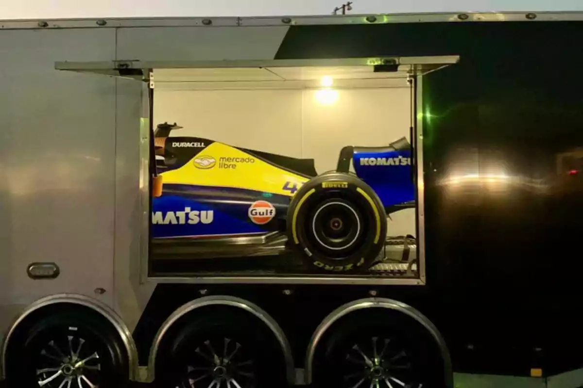 Un auto de carreras con colores azul y amarillo está guardado dentro de un remolque con la puerta abierta.