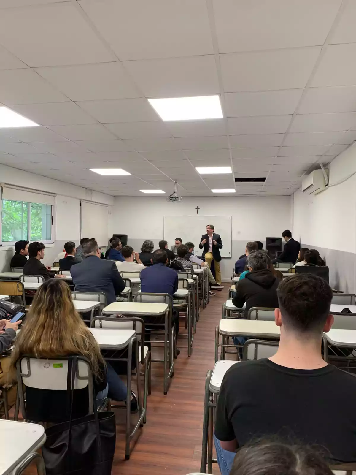 Un grupo de personas en un aula atendiendo a un orador frente a una pizarra.