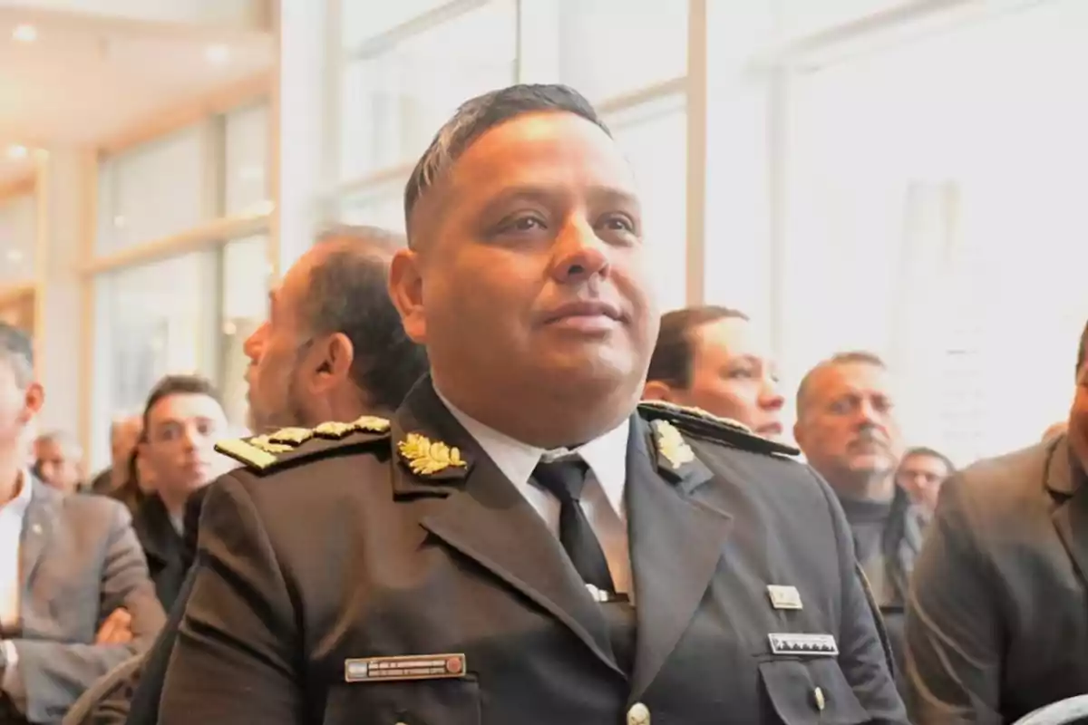 Un hombre con uniforme militar asiste a un evento en un salón lleno de gente.